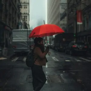 man in black jacket holding umbrella while walking on pedestrian lane during daytime